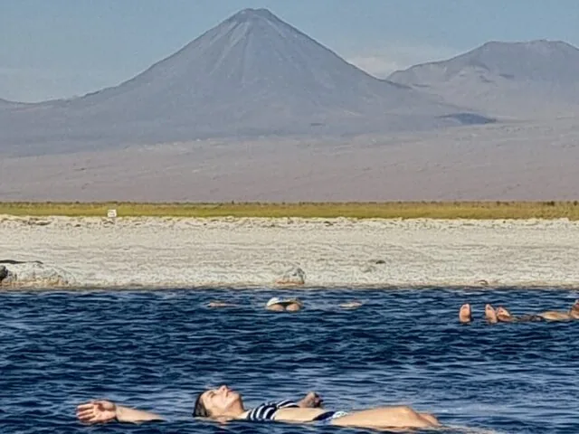 People floating in a dark blue salt lake with a volcano in background.