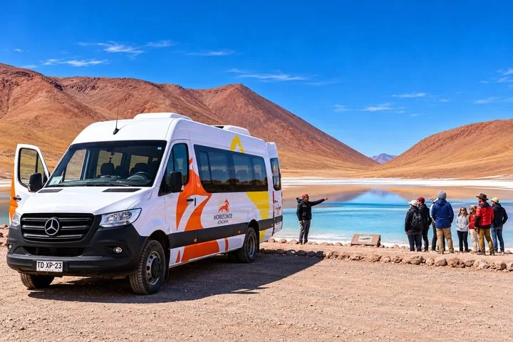 Tour group stands near a white van by a brightly colored lake.