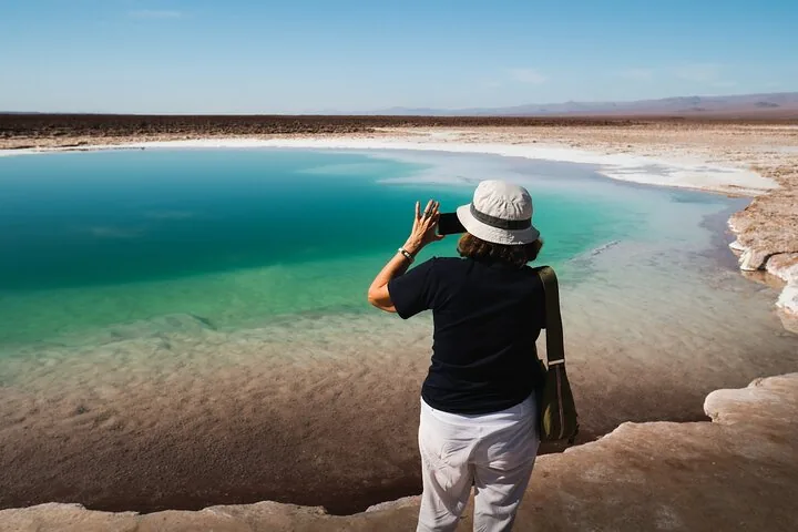 Turquoise pool surrounded by white salt flats and desert mountains.