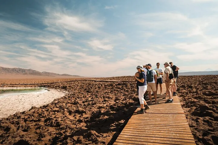 Woman taking a photo of a brilliant turquoise pool in a desert landscape.