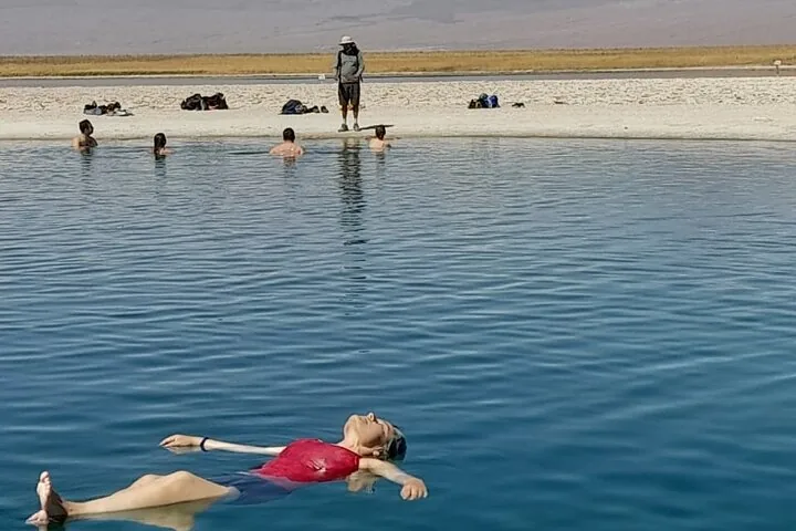 People swimming and floating in a vivid blue lake in a desert landscape.